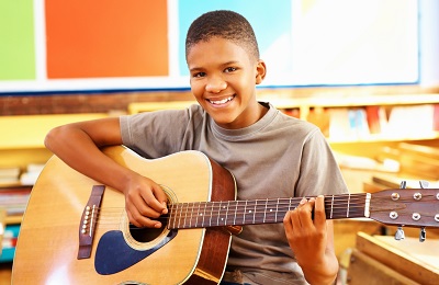 child with a smile holding
            a guitar